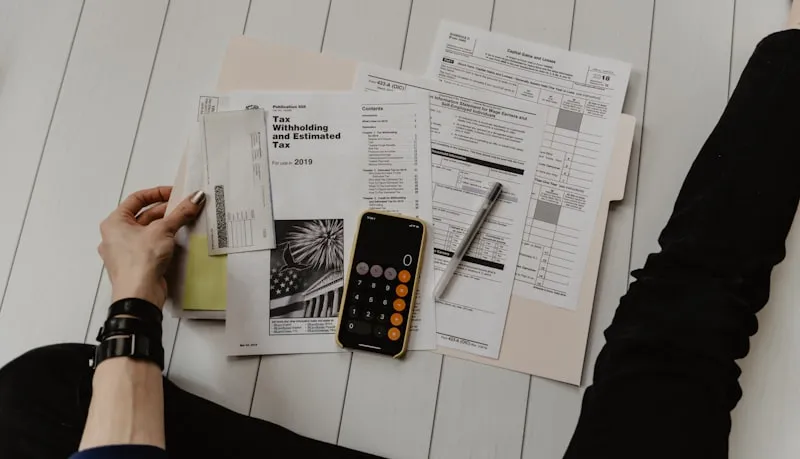 Hands sorting tax forms next to a calculator and a phone