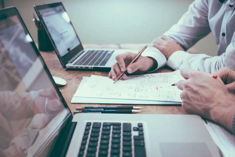 Two people at a desk with laptops and paper plans